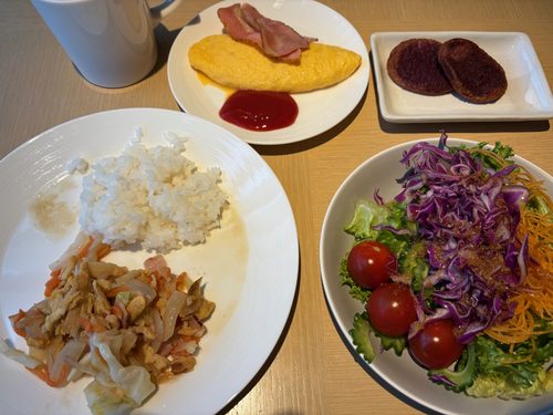 朝食ビュッフェのプレート。サラダ、炒め物、ごはん、オムレツとベーコン、紅いもの菓子